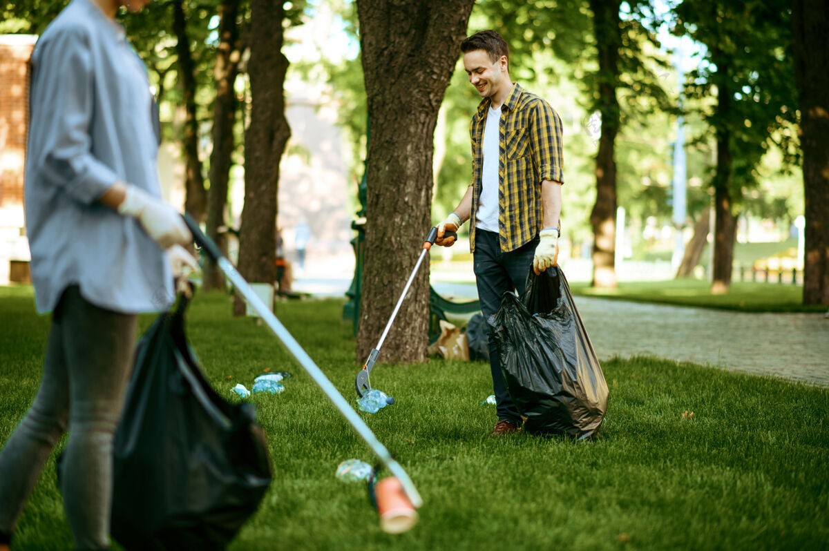 垃圾箱两个男人在公园里用袋子收集塑料垃圾 做义工袋子清洁保护