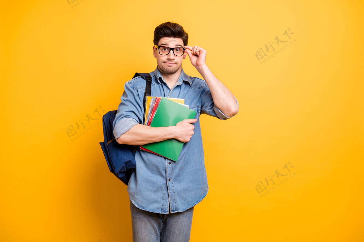 学习照片中害羞犹豫的好人戴着眼镜 背着背包 手拿着文案 隔离着鲜艳的黄色墙壁记事本胡茬极客