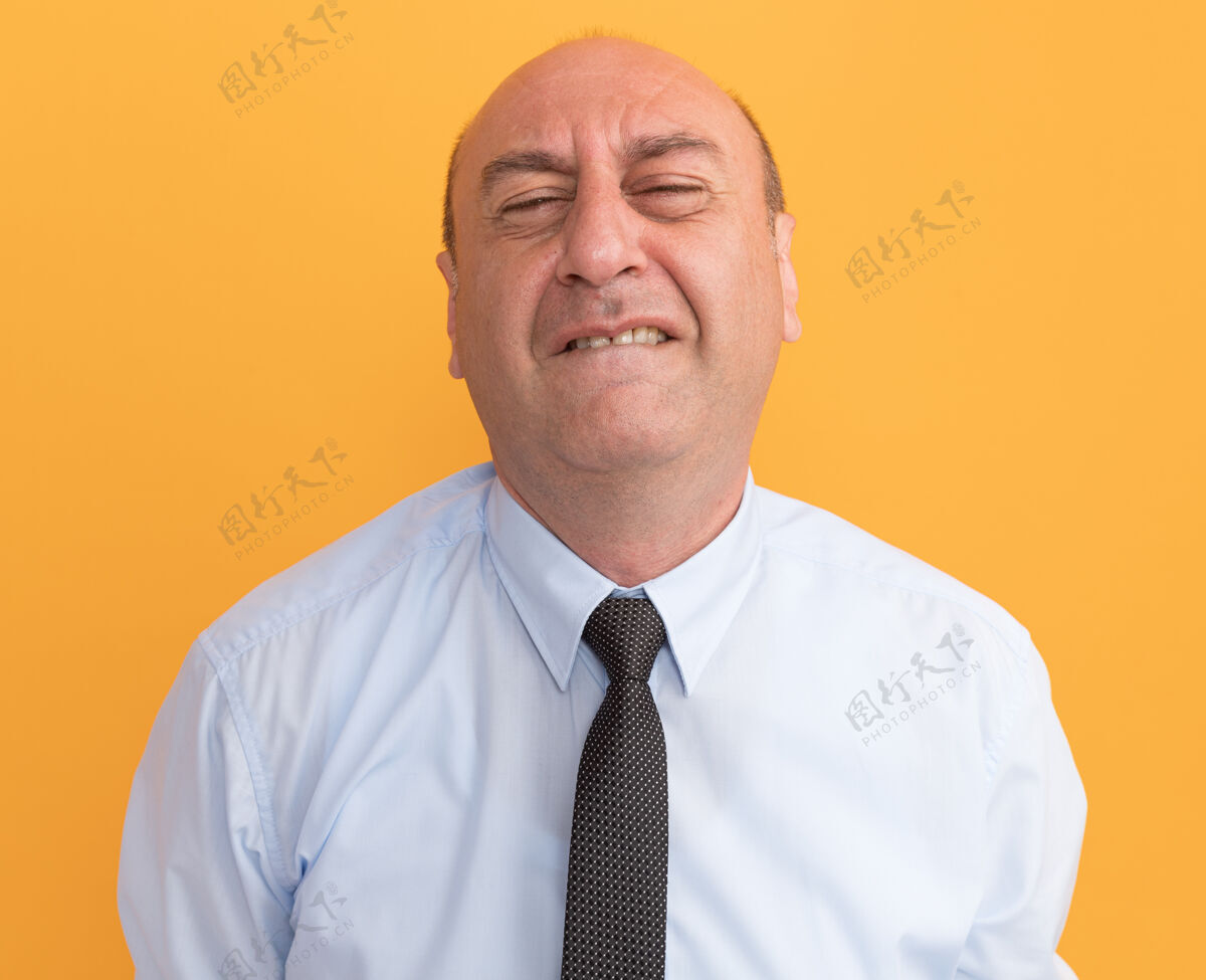 眼睛紧闭双眼紧张的中年男子穿着白色t恤 打着领带 隔离在橙色的墙上人脸姿势