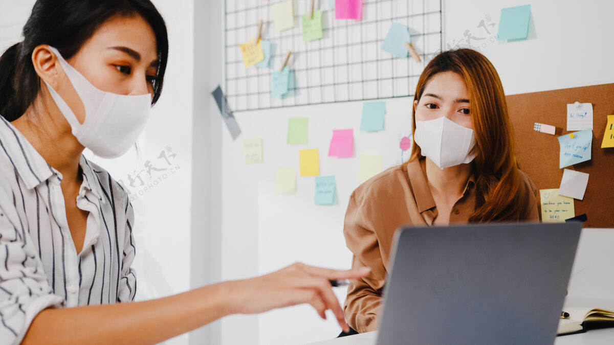 距离亚洲商务人士利用电脑演示会议集思广益 讨论新项目同事的想法 并戴上防护面罩回到新的正常办公室流行病社交预防