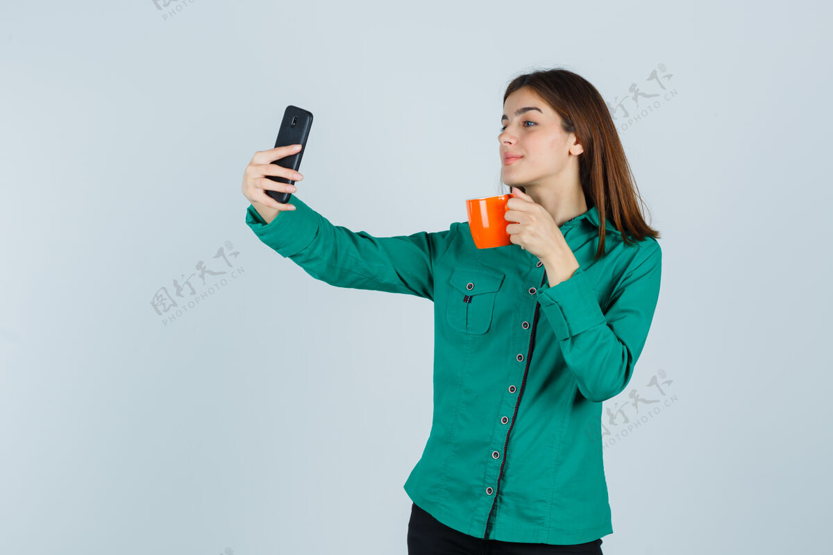 治疗年轻的女士拿着桔黄色的茶杯 穿着衬衫拿着手机自拍 看起来很自信 正面照护理自拍女人