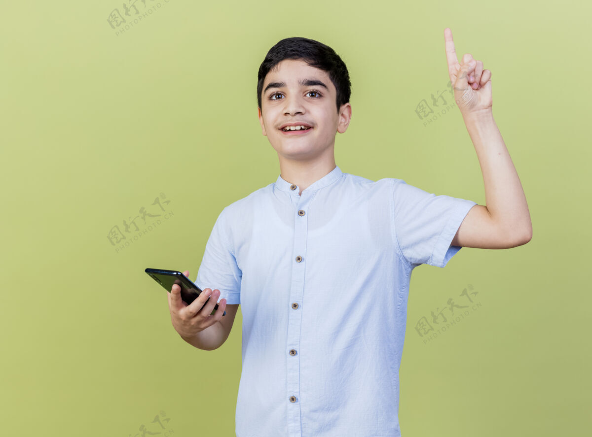 拿着印象深刻的小男孩拿着手机看着前面指着孤立的橄榄绿墙上印象人市民