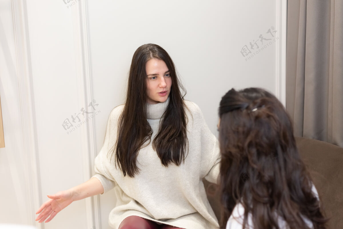 成人年轻女子在美容师医生的招待会上 两名女子坐在沙龙的沙发上交流 选择一个程序专业皮肤女人