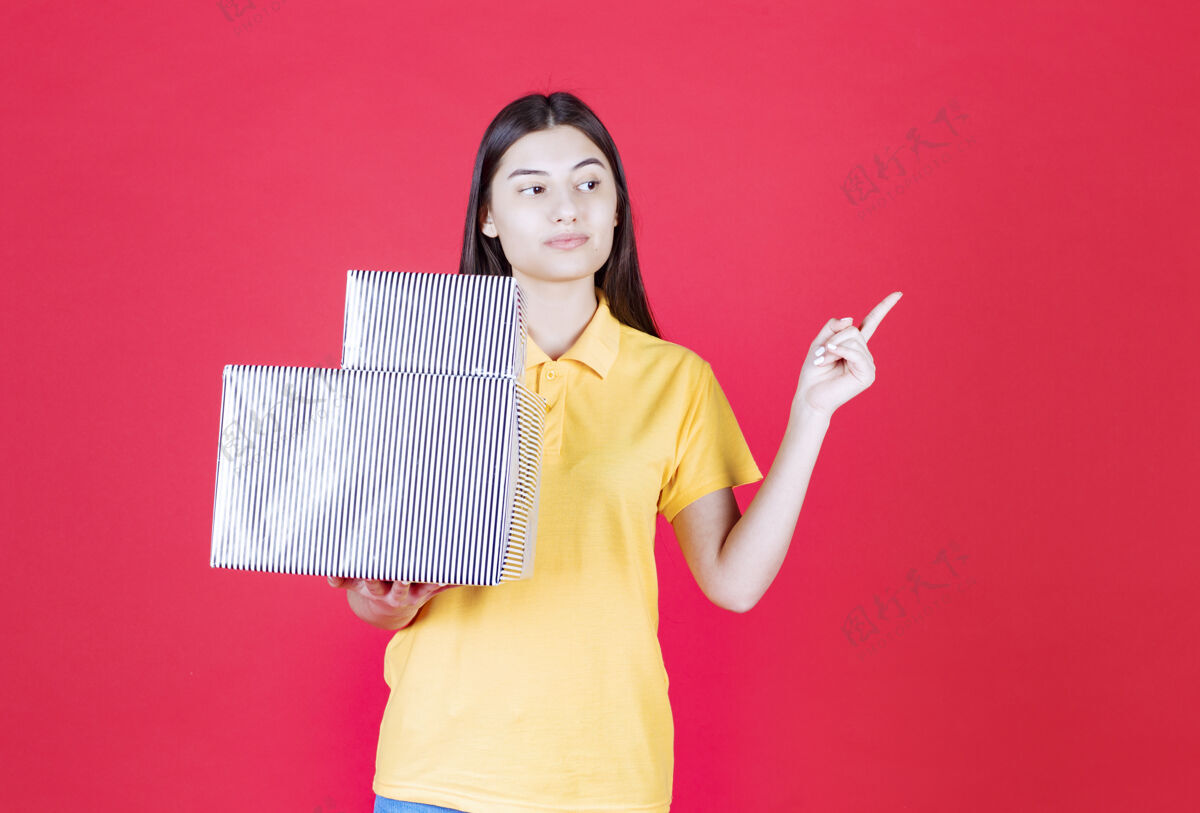 人一个穿着黄色衬衫的女人手里拿着一个银色的礼盒 看上去很困惑 很有思想礼盒生日不确定
