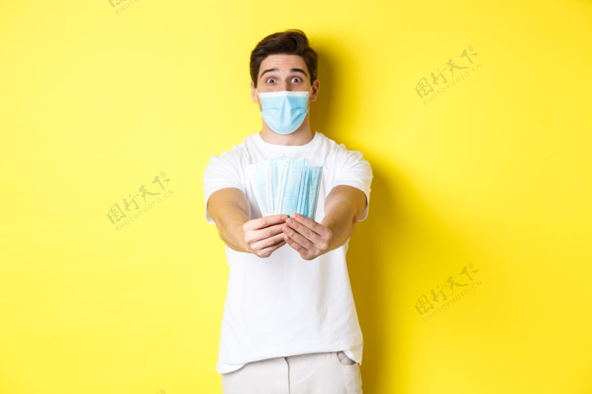 时尚covid-19的概念 检疫和预防措施年轻的高加索男子给你的医用口罩 站在黄色背景下面膜男性演播室