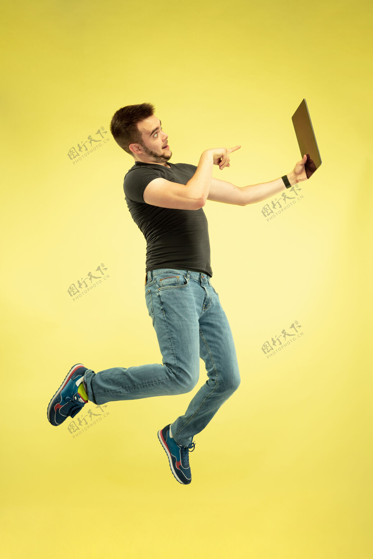 显示失重全长的快乐跳跃的人与黄色背景上孤立的小玩意画像电话笔记本电脑设备