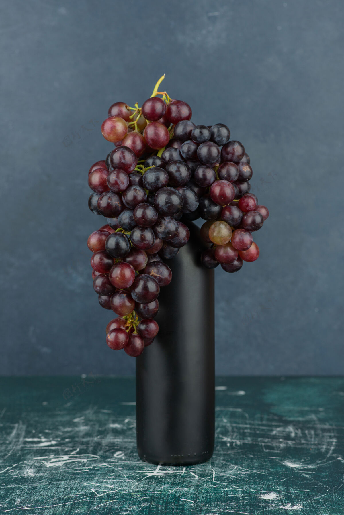 黑色大理石桌上的一个瓶子周围有一簇黑葡萄成熟瓶装葡萄