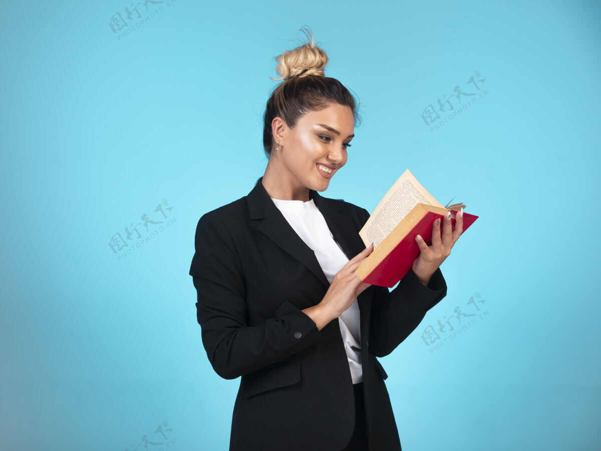办公室穿着黑色西装的商务小姐拿着一本红色的书 正在读呢工作积极笔记本