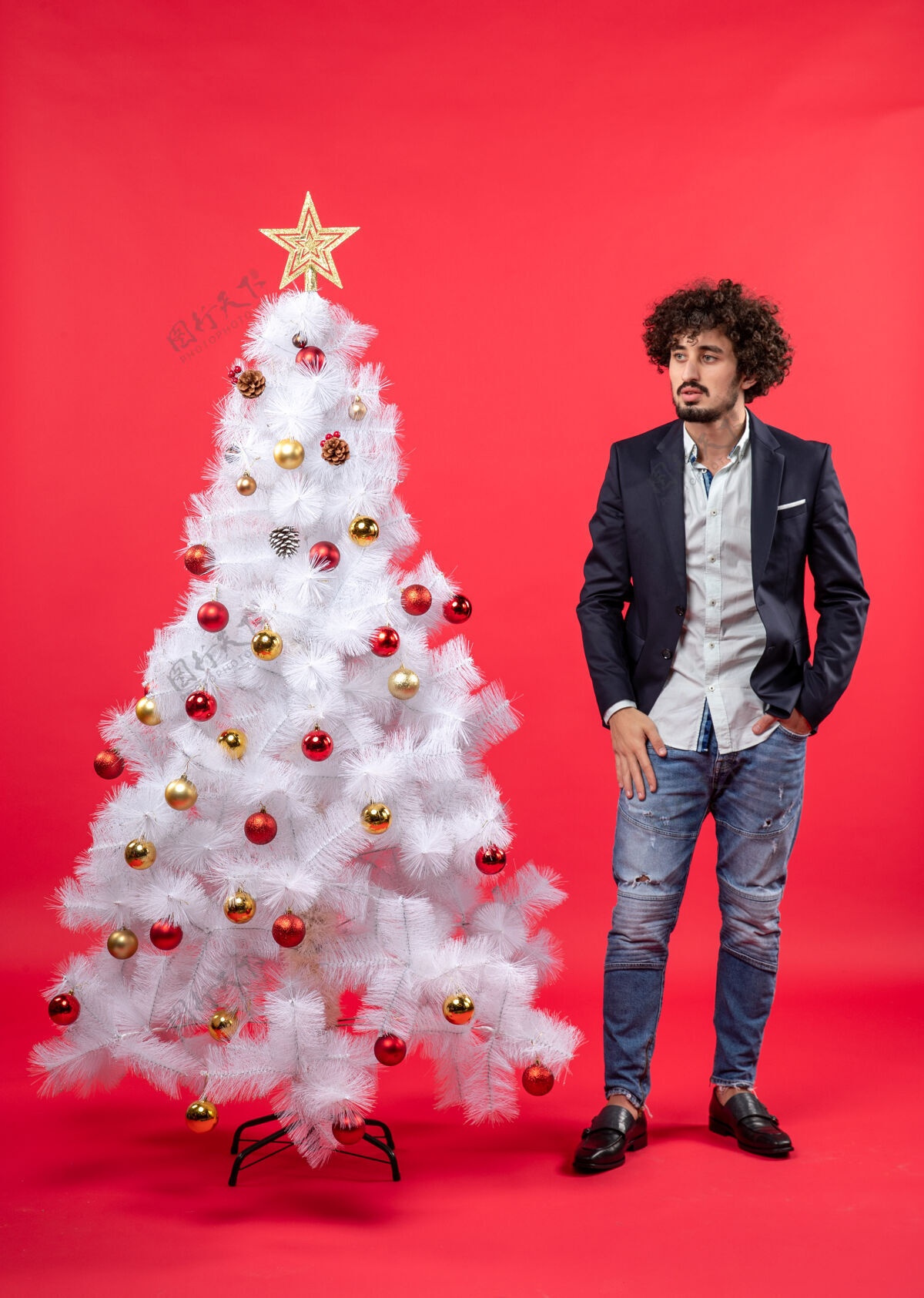 快乐圣诞庆典上 留着胡子的年轻人站在圣诞树旁看着什么东西装饰庆祝东西