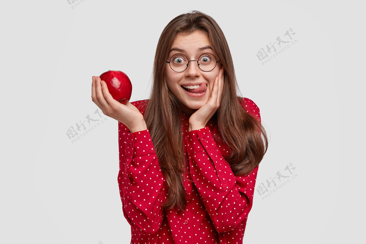 黑发室内拍摄的美女捧着新鲜多汁的苹果舔嘴唇 很有意思 穿着优雅 喜欢吃维生素眼镜水果多汁