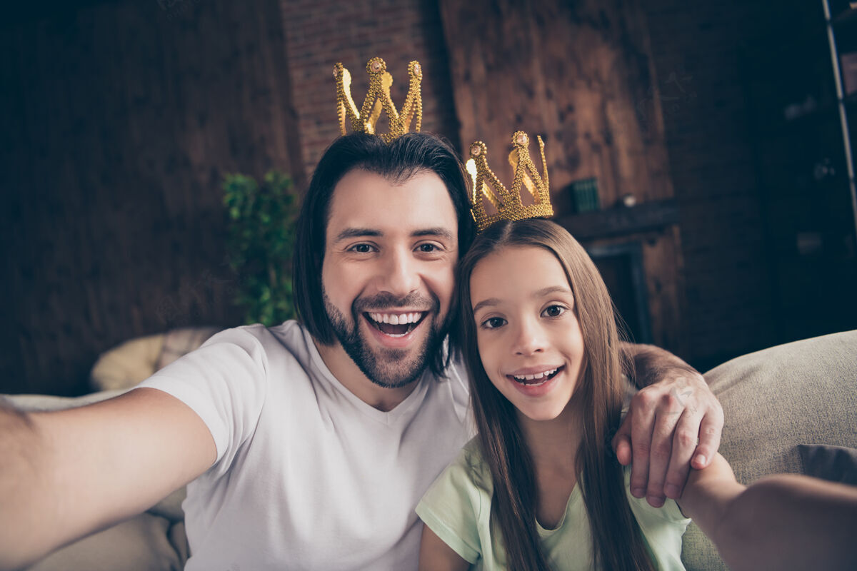 父母美丽可爱的小女孩和英俊年轻的爸爸坐在舒适的沙发上的照片国王朋友皇冠