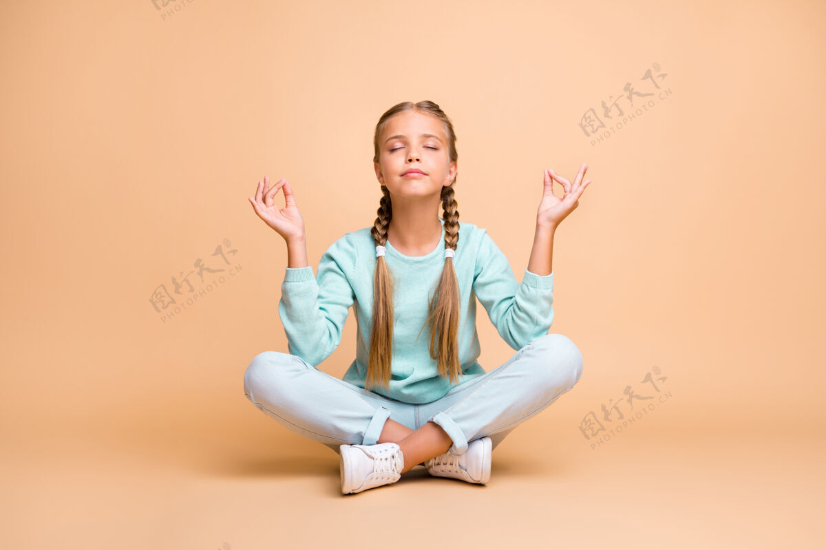 莲花美丽的小女士坐在地板上腿交叉眼睛闭着手指一起莲花位置冥想穿蓝色毛衣牛仔裤鞋隔离米色墙体位咒语孩子