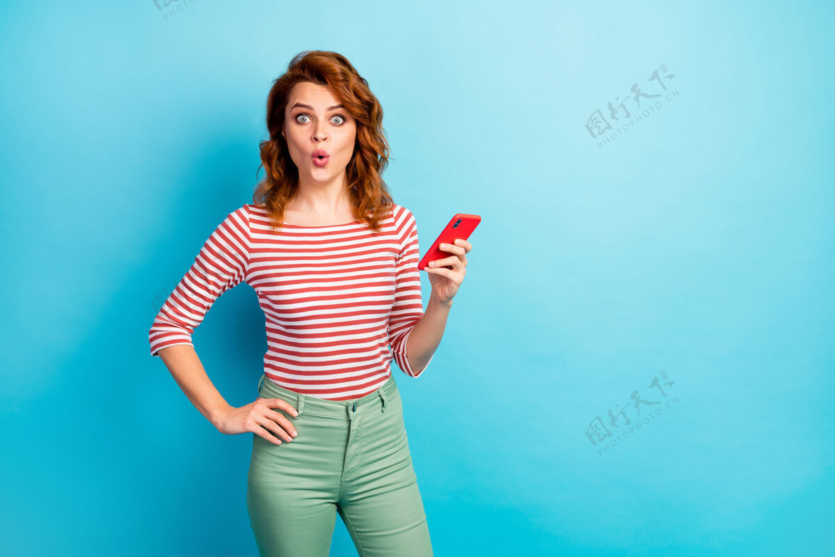 惊人惊讶的女人的肖像使用智能手机得到社会媒体通知印象深刻尖叫哇天哪穿好看的毛衣蓝色隔离在线反应电话