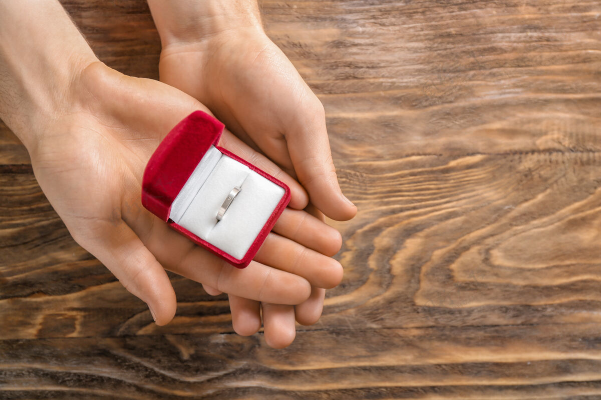 浪漫木桌上的男性手持订婚戒指的盒子成人盒子木头