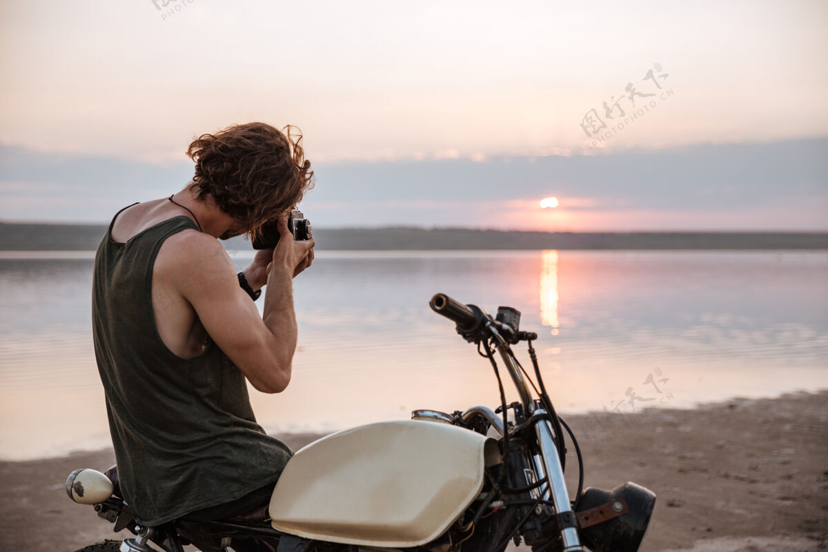 摩托车手坐在户外摩托车上用相机拍照的年轻人高加索照片日落