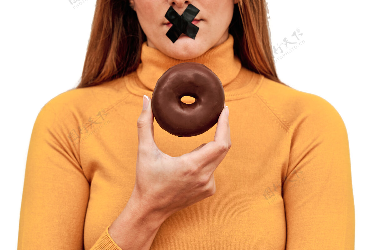 决心一个面目全非的女人的前视图 她的嘴上缠着胶带 手里拿着一个甜甜圈女性年轻甜甜圈