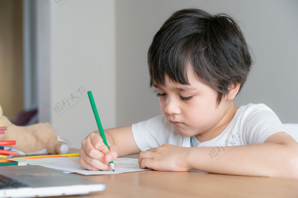 家庭作业脸上带着不开心的孩子做作业 无聊的孩子用绿色铅笔着色房子男孩快乐