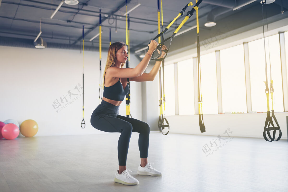 悬挂美丽的年轻女子训练与悬挂教练吊索或吊带在健身房教练运动女孩