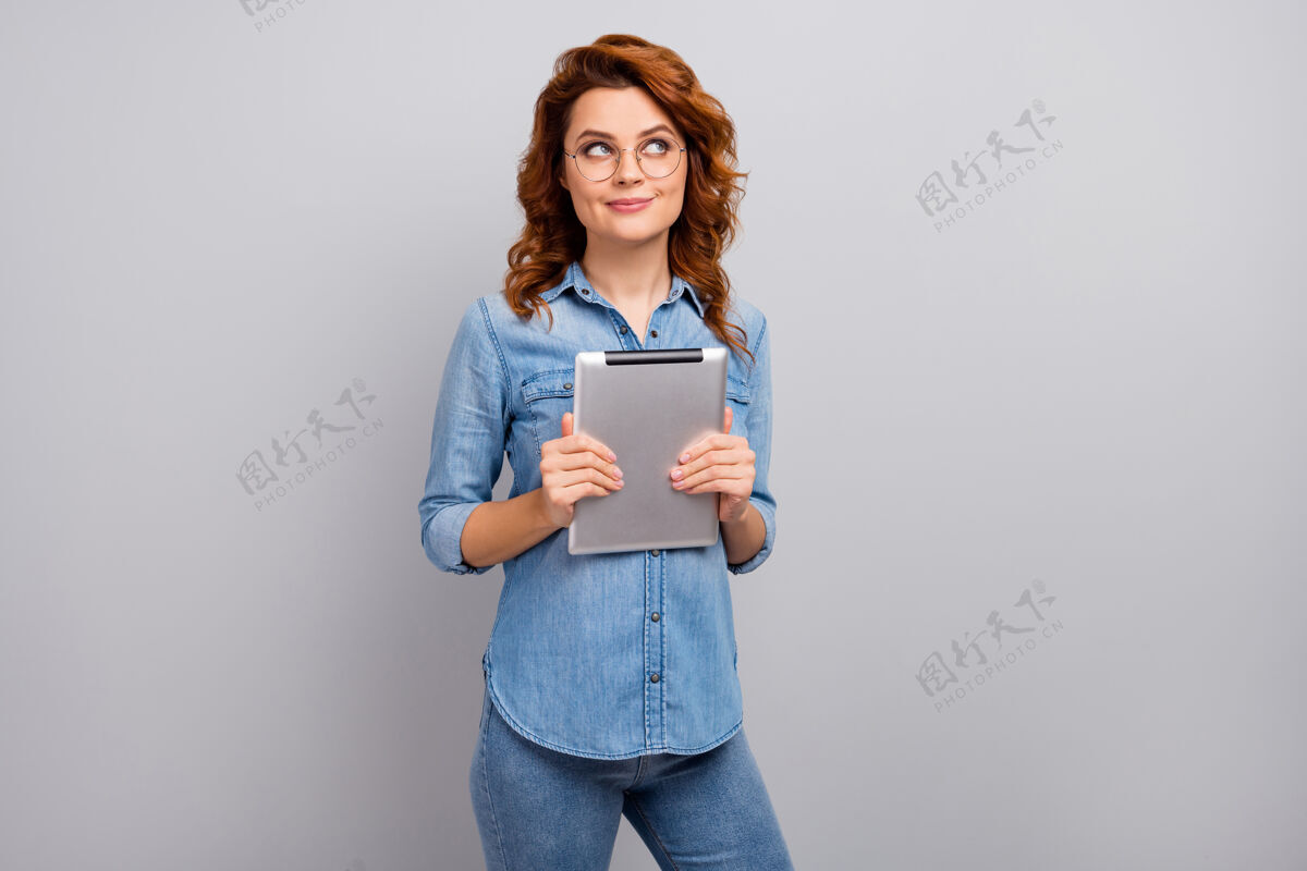 自由职业者有兴趣的女人的肖像拿着使用平板电脑思考想法看文字空间决定社交媒体应用后穿现代服装隔离灰色墙壁休闲女人牛仔裤