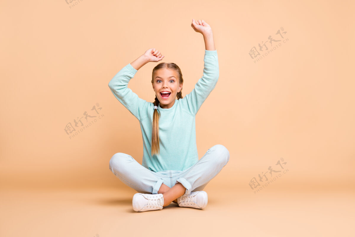 小目标全身照片美丽的小女士举起拳头看体育比赛兴奋的球迷坐地板腿交叉穿蓝色毛衣牛仔裤鞋孤立米色墙快乐鞋休闲