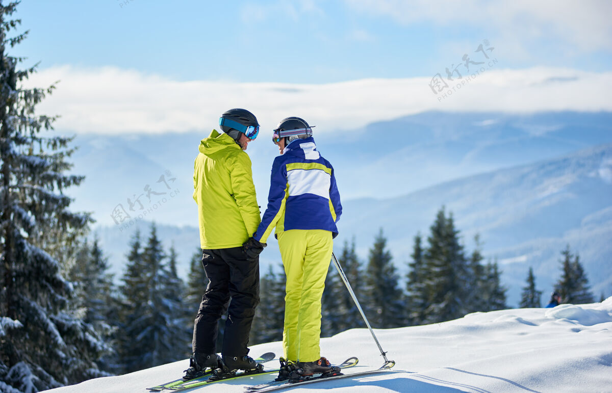 配对背影：快乐的情侣滑雪者站在山边 手牵着手 欣赏冬日山景的全景回来男人杉木