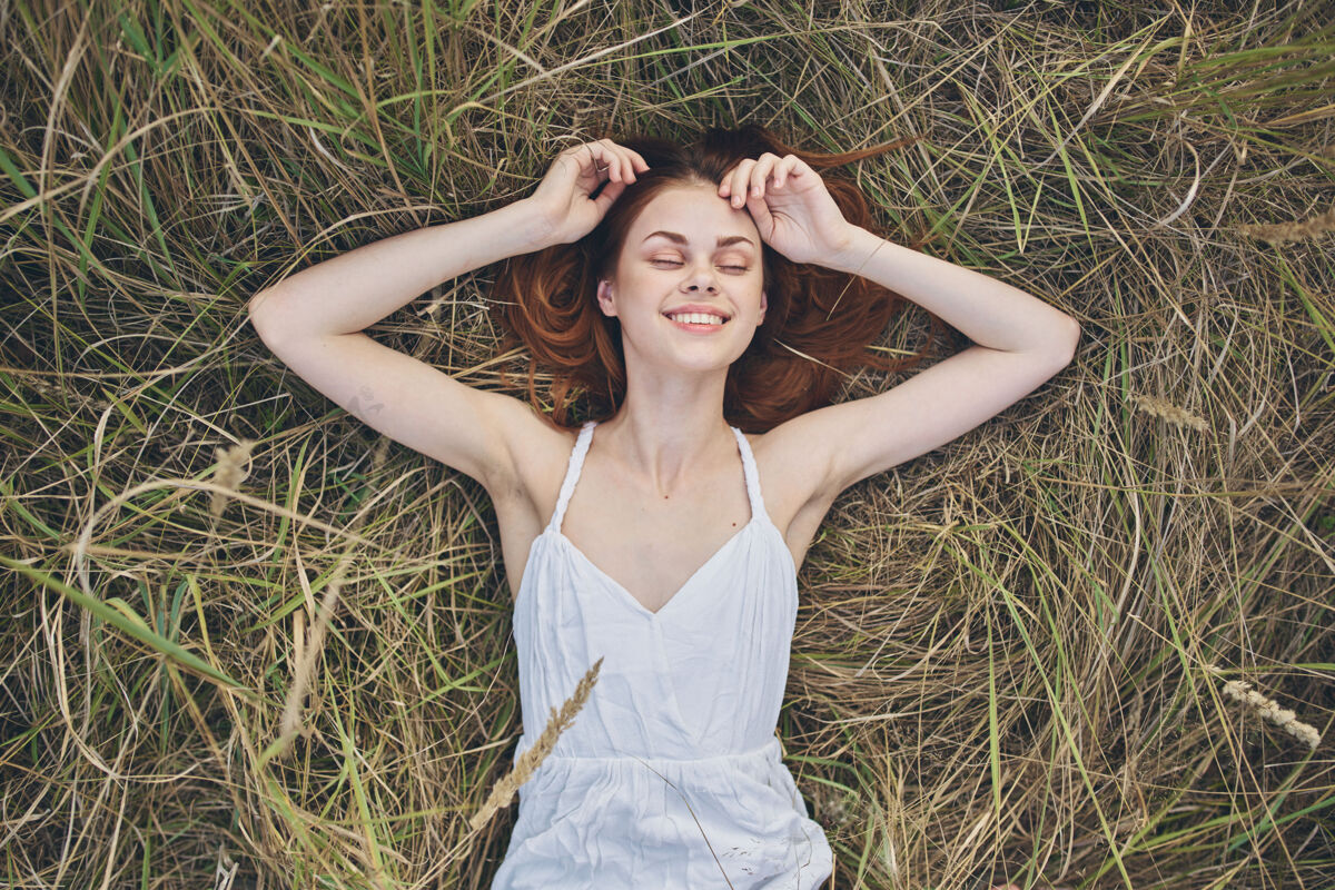 手快乐的女人躺在干草上 用手比划着白色的裙子美丽植物户外