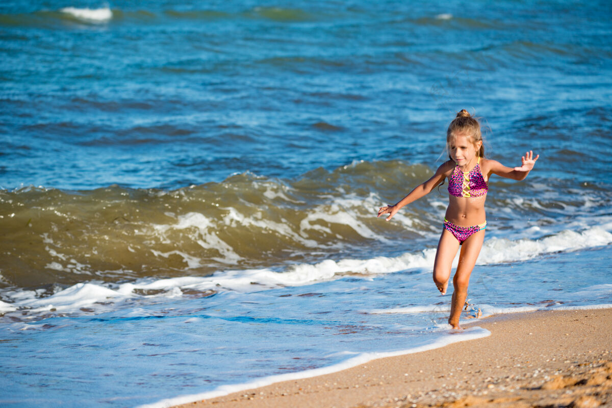 明亮在一个阳光明媚温暖的夏日 快乐的小女孩在平静的海浪旁的沙滩上奔跑奔跑坠落欢呼
