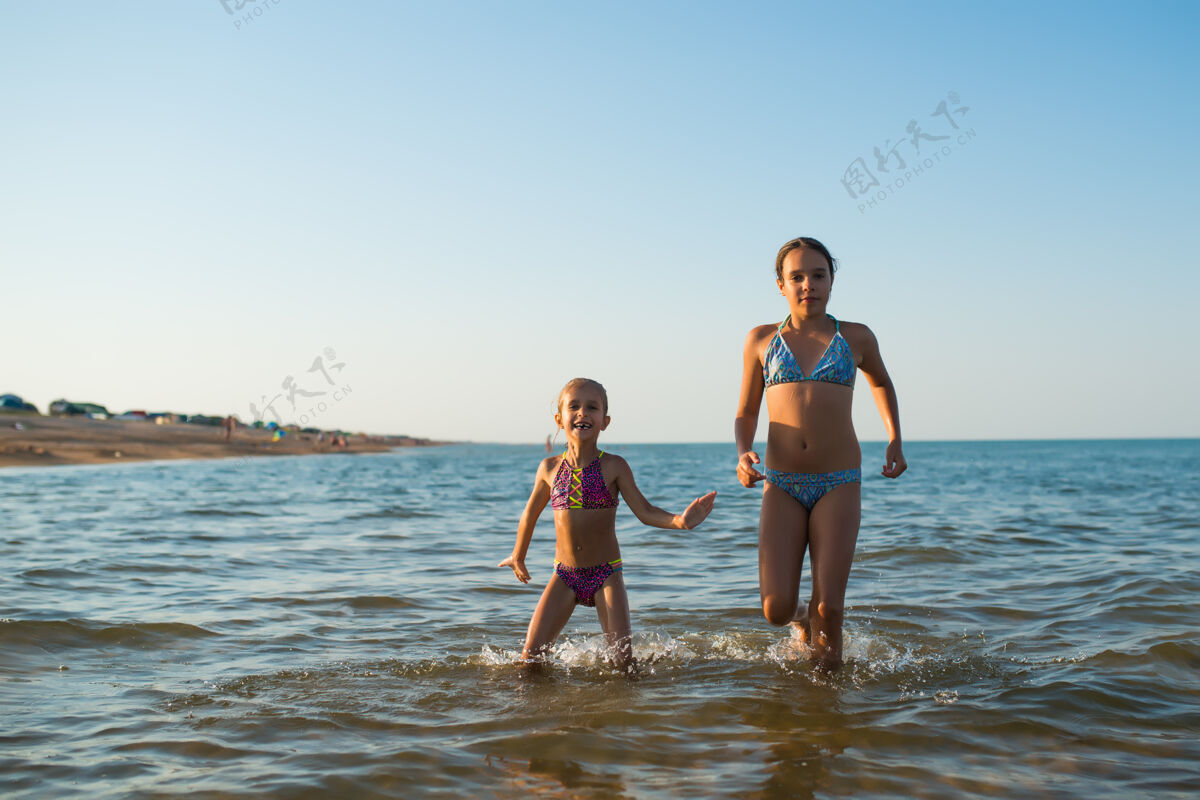 海岸在一个阳光明媚的炎炎夏日 两个快乐而积极的女孩姐妹在度假时沿着海浪奔跑欢笑刮风太阳