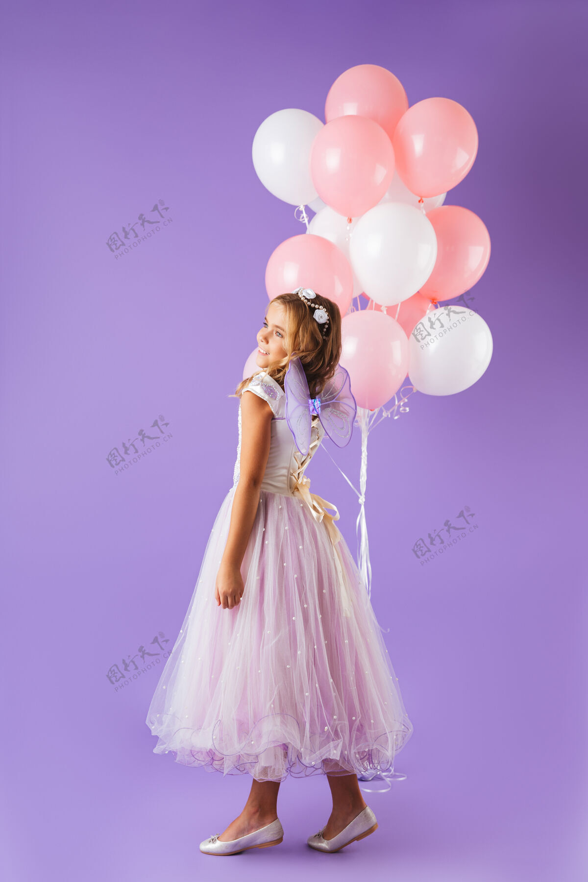 五颜六色一个穿着公主裙的漂亮小女孩孤零零地站在紫罗兰色的墙上 手里拿着一堆气球连衣裙肖像童年
