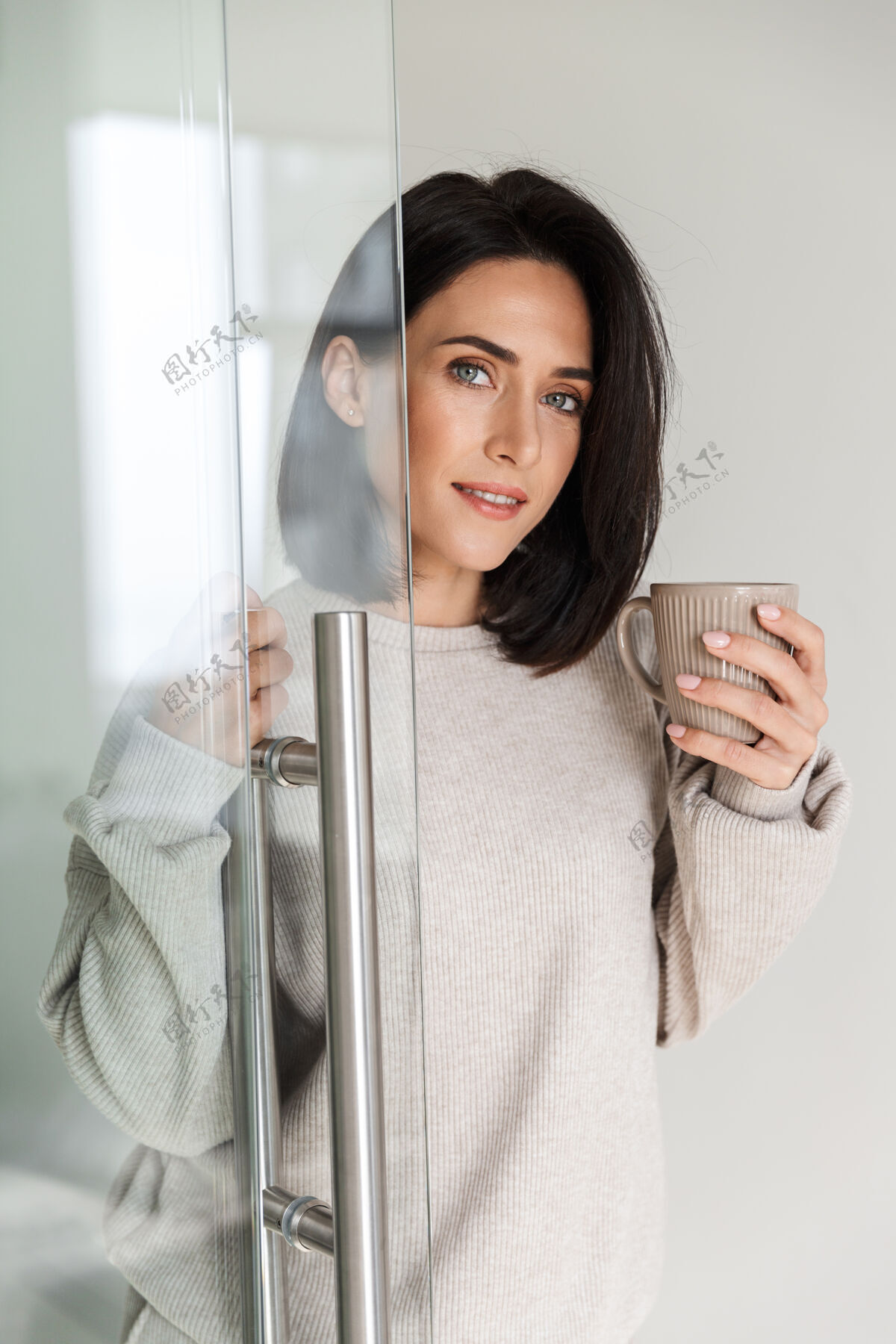 深色头发一个30多岁的黑发女人拿着茶杯 早上站在现代明亮的房间里白种人沙发室内