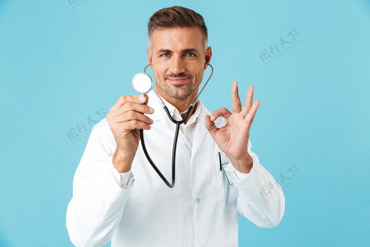 表情穿着白色制服手持听诊器的欧洲医生的画像 孤立地站在蓝色的墙上专业知识积极治疗
