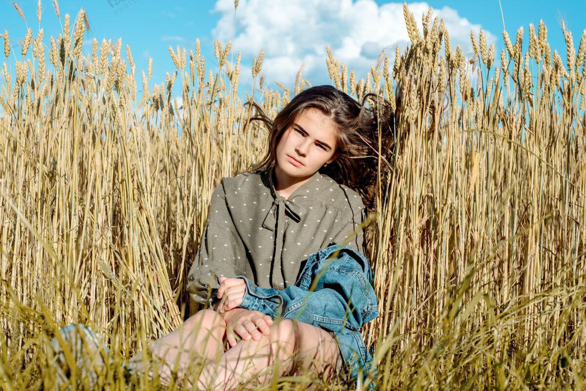 风景穿礼服的漂亮女孩模特反对田野的背景小麦蓝天空 自由和炎热的夏天的概念肖像女士美丽