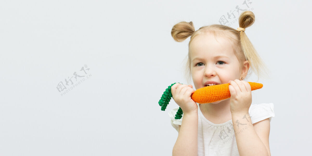 小小女孩正在吃白色背景上的玩具胡萝卜健康食品女孩小食物