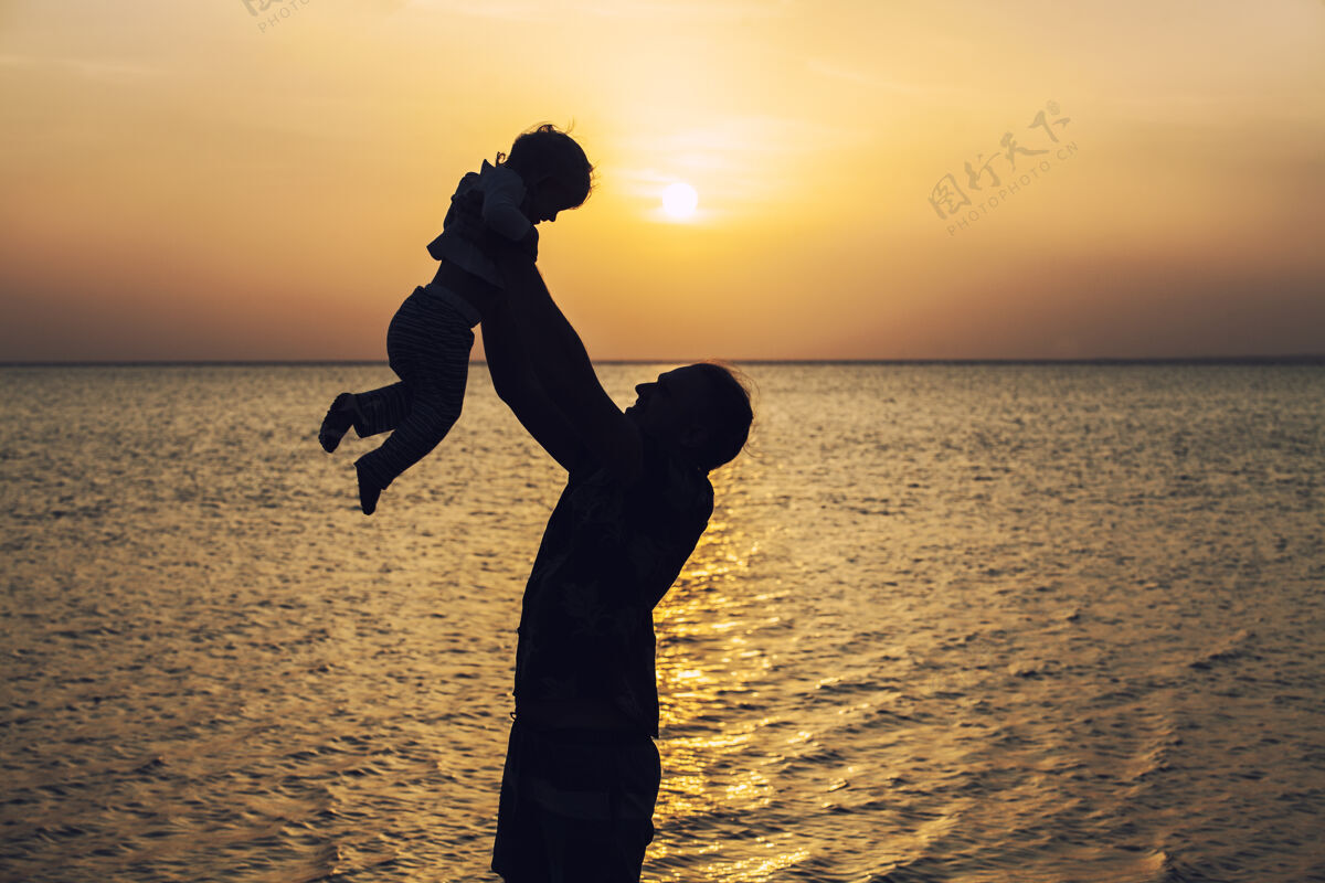 黎明父亲把孩子的剪影扔在黎明和清晨的大海的背景上日落夜晚活跃
