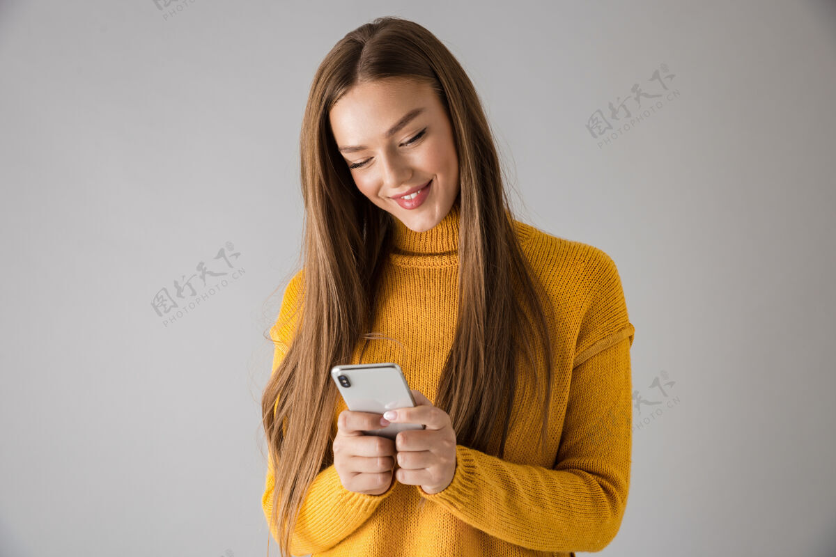 爱一个美丽快乐的年轻女子用手机隔着灰色的墙被孤立的画面成人休闲时尚