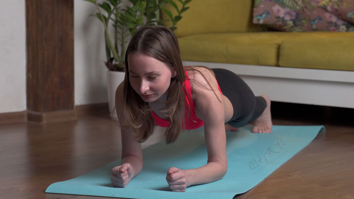 健康穿着运动服的漂亮年轻女子晚上在家里的瑜伽垫上做平板运动人力量活动