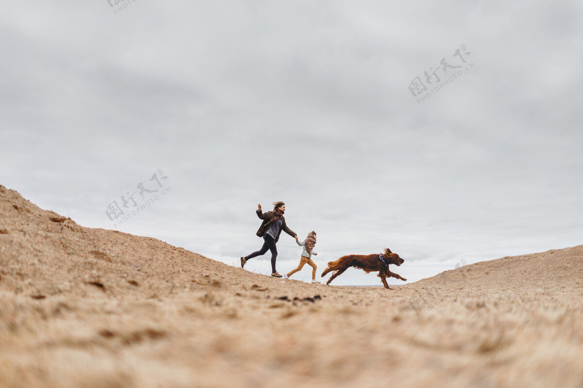狗幸福的家庭和他们的狗在沙滩上奔跑海滩妈妈儿子和一只狗在街上玩玩耍生活背部