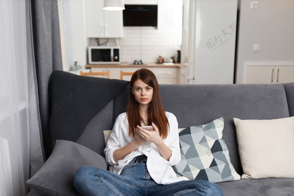 坐着手拿手机坐在舒适沙发上的女人休闲周末科技年轻美容房间