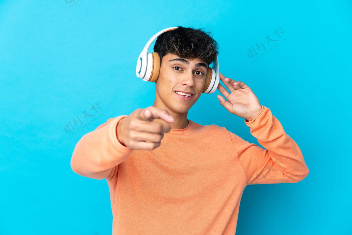 耳机年轻人越过孤零零的蓝色墙壁 一边听音乐 一边指着前面指向歌曲家伙