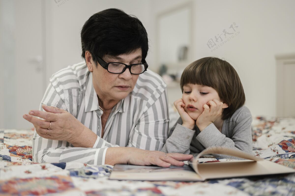 小奶奶和孙子在家看书的正面图男孩阅读女性