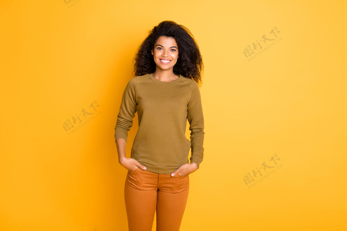 自信迷人可爱开朗的好女朋友手牵手在口袋里穿着橙色的裤子在生动的色彩背景下孤立的照片美式女性美丽