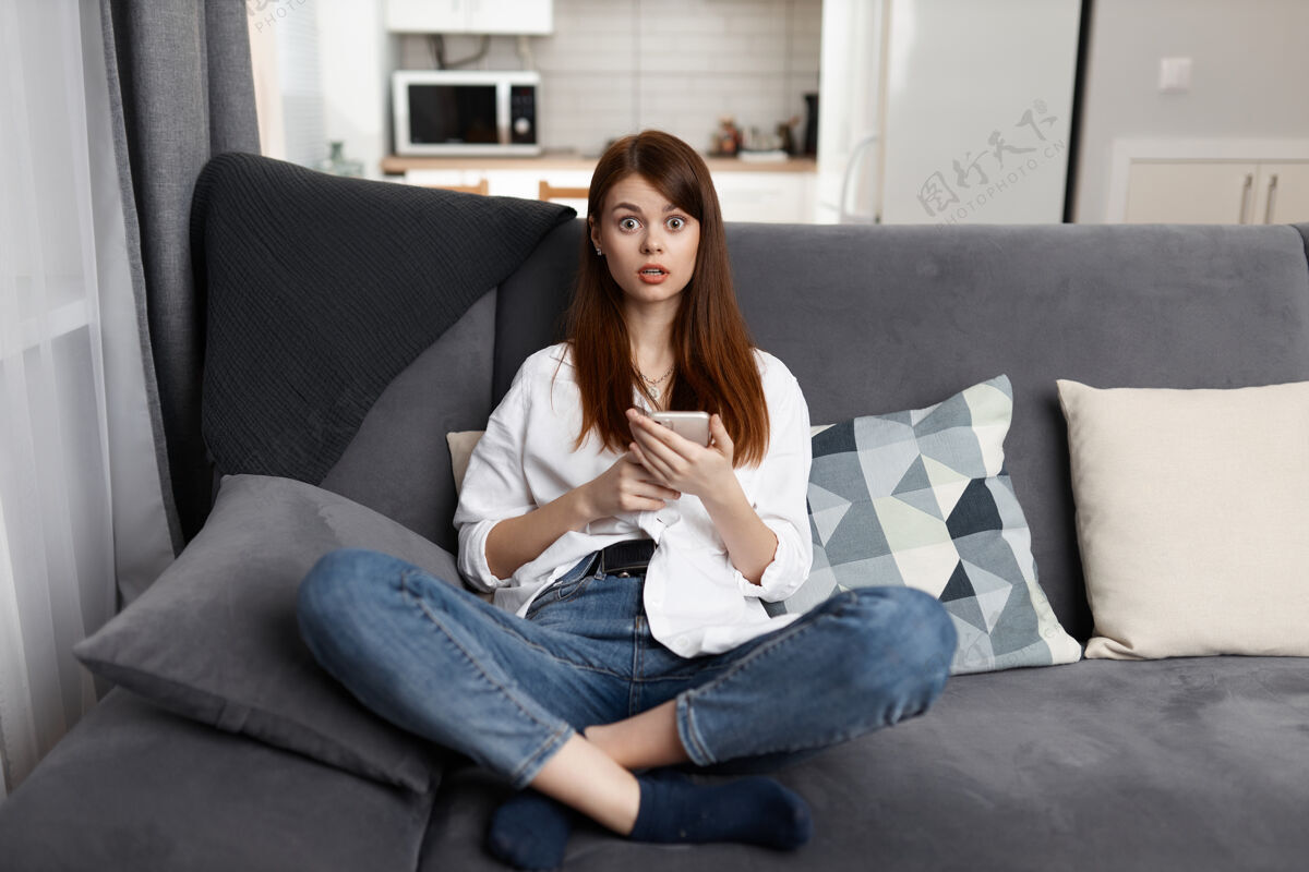 客厅一个手拿电话坐在舒适的沙发上的女人在家里的生活方式让人惊讶连接生活便携式