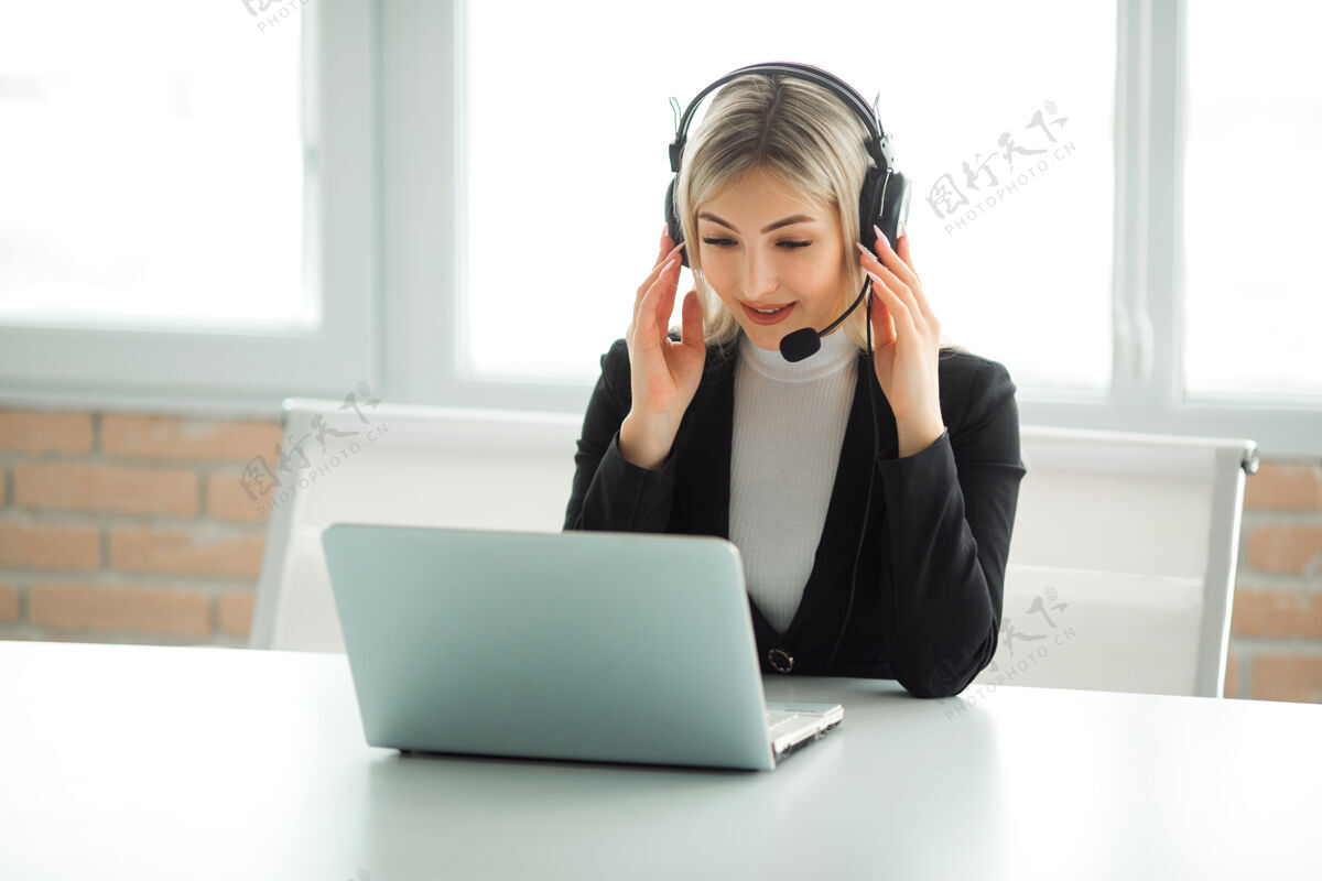 技术一个穿着西装的漂亮年轻女子坐在办公室的桌子旁 手提电脑插着耳机专业经理行政人员