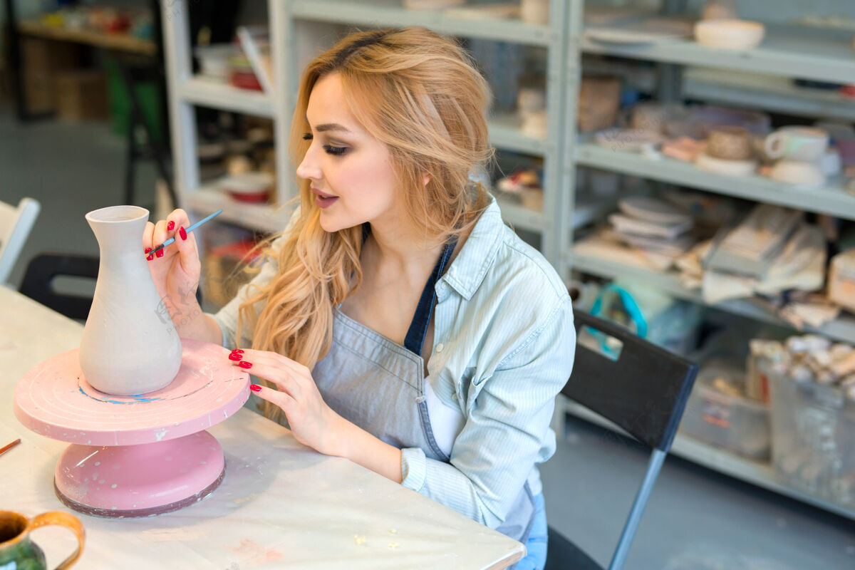 漂亮美丽的年轻女子在陶艺作坊里画陶罐微笑制造Moldura