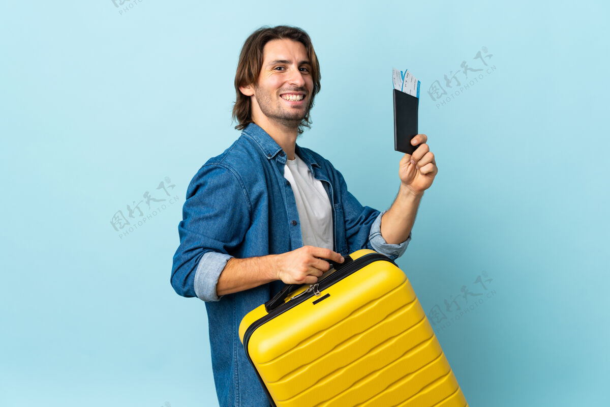 手提箱年轻帅哥带着手提箱和护照被隔离在蓝色的墙上度假模型帅哥家伙