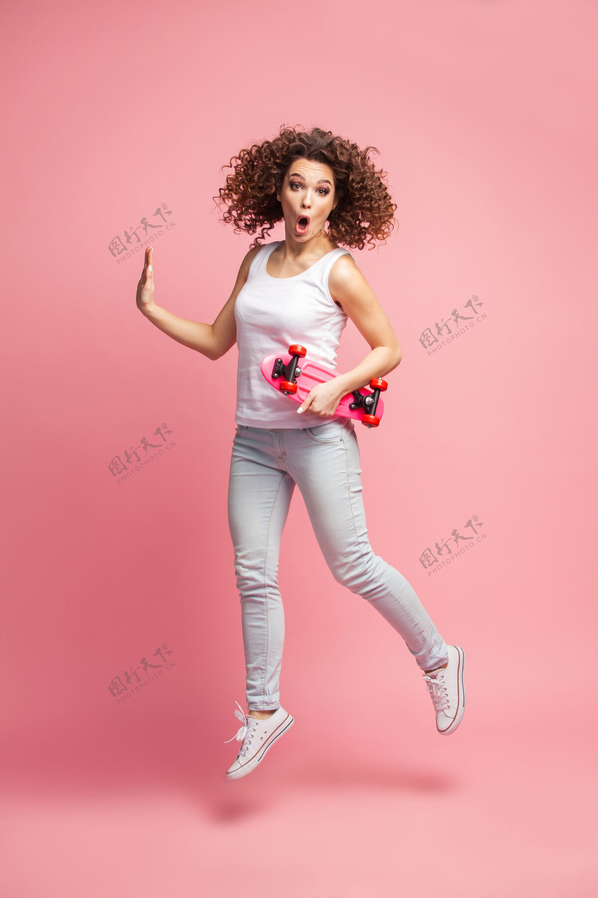 漂亮一个穿着夏装的美丽快乐的女人的全长肖像摆姿势 看着远处 一边跳着 一边拿着粉红色的滑板离开持有滑板