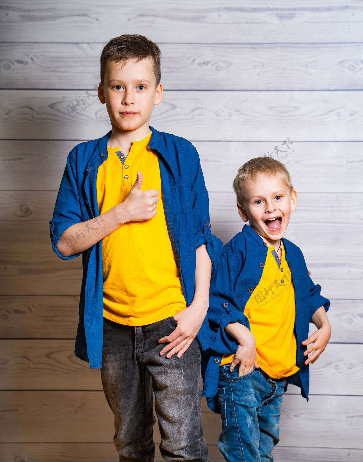 童年两个穿着蓝色衬衫和黄色t恤的帅哥在一起摆姿势手臂微笑手