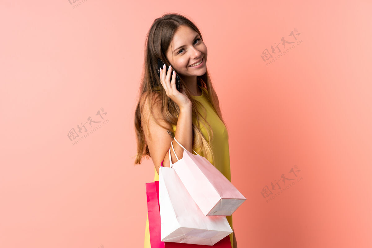 粉色一位年轻的立陶宛妇女 手拿购物袋 拿着手机给朋友打电话 被隔离在粉色背景下购物女士金发