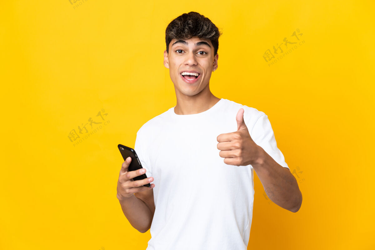 微笑年轻人在孤立的黄色背景下一边用手机一边竖起大拇指交谈沟通手机