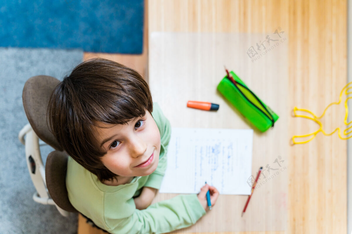 青少年小男孩坐在桌子旁做作业家集中儿童写作练习很高兴在家上学概念坐着房间人